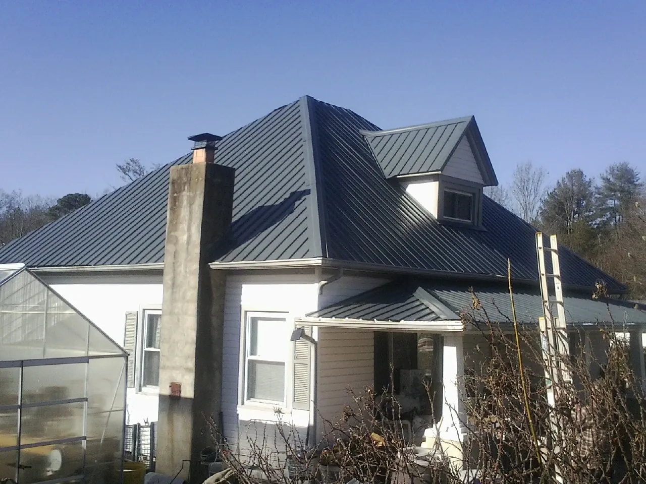 Dark blue standing seam metal roof on a white farmhouse with dormer — Slate & Tile Roof Repair by Roofing Brothers in Weiser