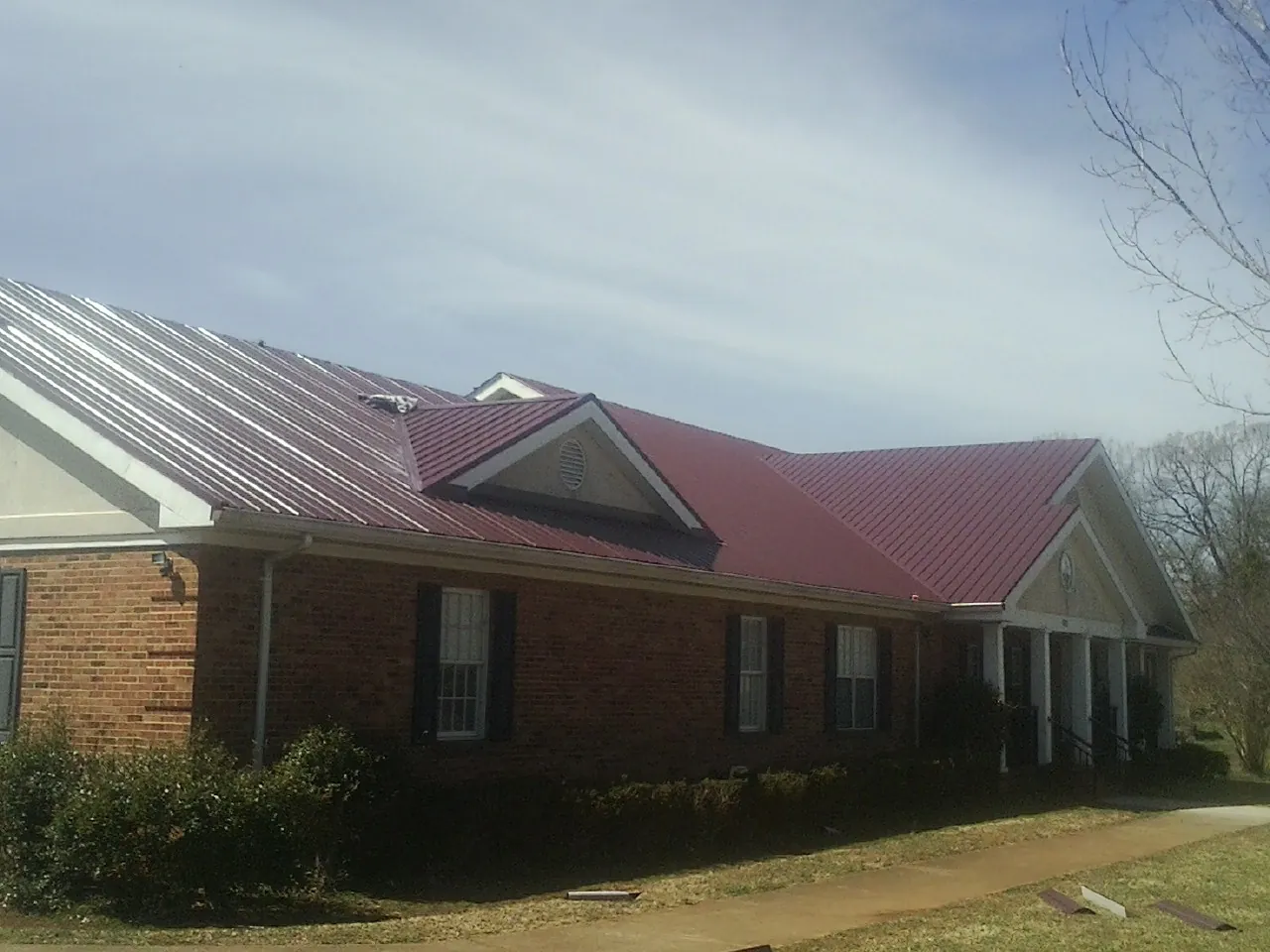 Red metal roof with gabled entries on a long brick building, from a Hail Damage Roof Repair job in Weiser