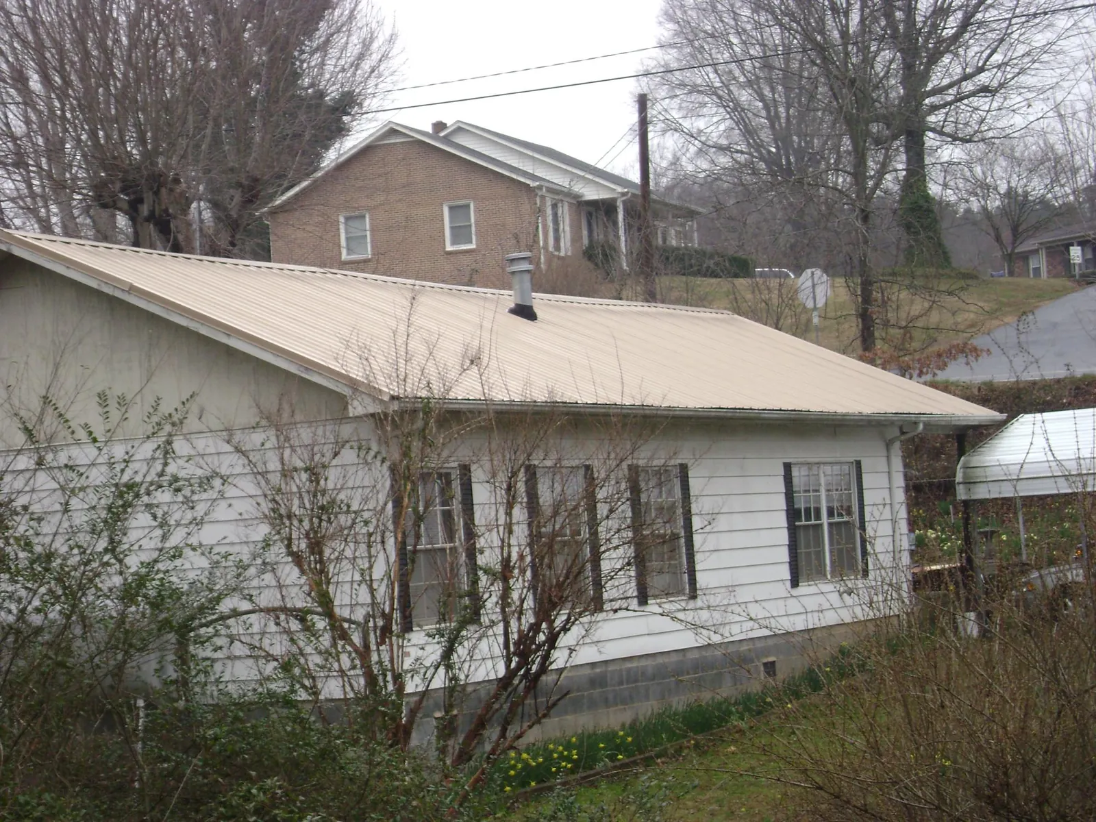 Tan metal roof on a white sided house set into a hillside — Commercial Roofing by Roofing Brothers in Weiser